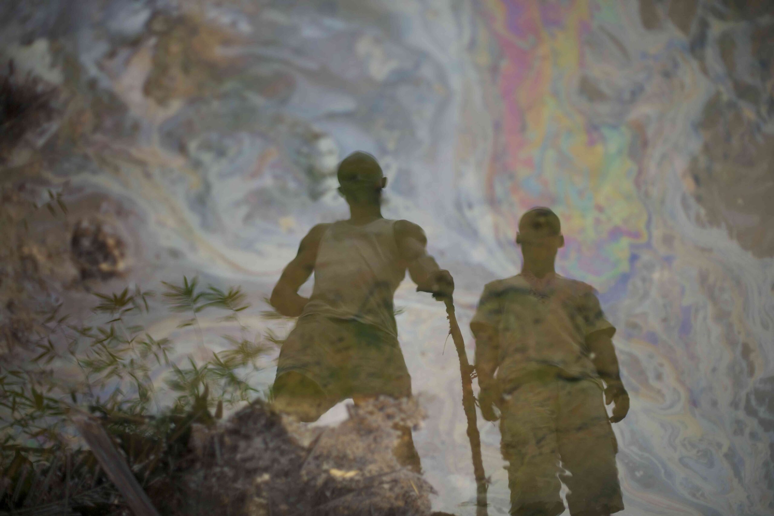 reflection of two men in oil-tainted water