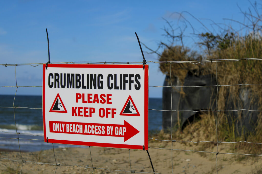 Sign reading 'crumbling cliffs' in front of a seaside background