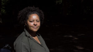 A woman dressed in a grey shirt looks at the camera