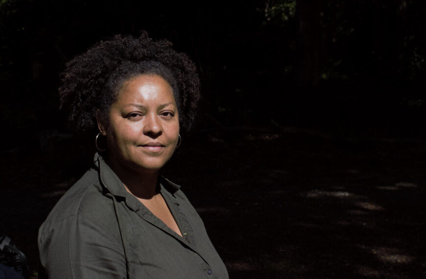 A woman dressed in a grey shirt looks at the camera