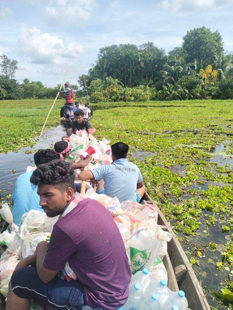 Volunteers carry supplies in two narrow wooden boats through an overflown river