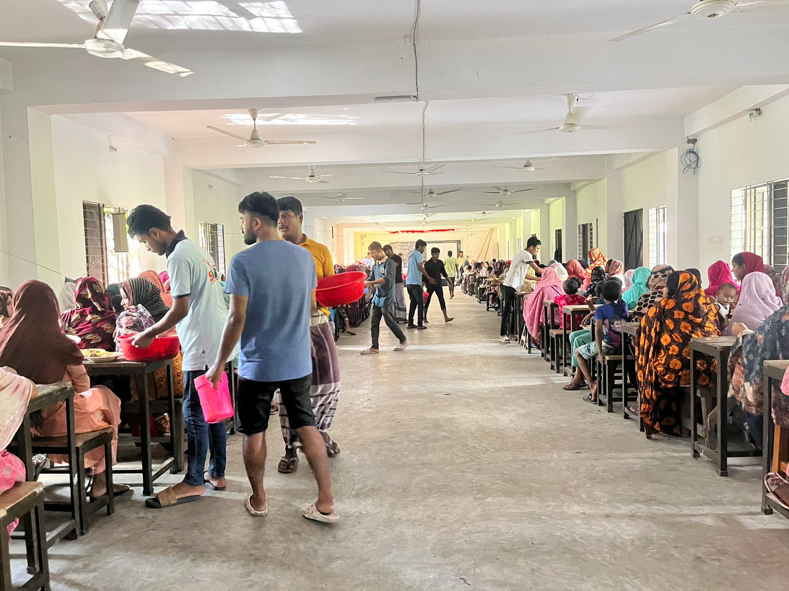 Hundreds of people eat at a community kitchen while the young volunteers serve food
