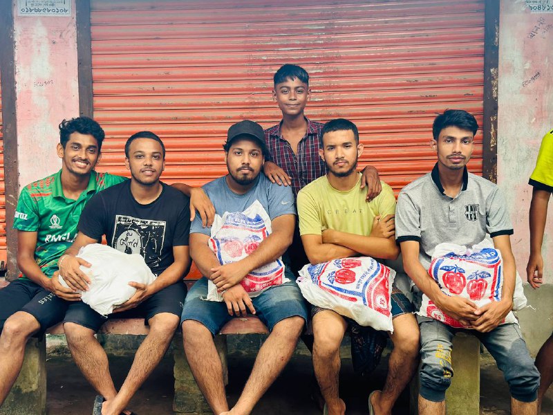 Six young men pose for a group photo while holding bags of supplies