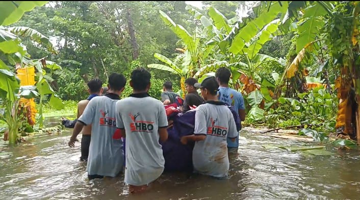 A group of young volunteers wearing SHBO t-shirts carry supplies, with water almost up to their waists