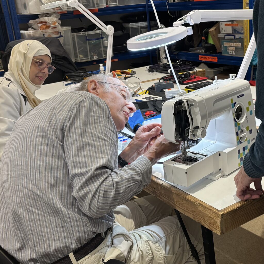 A woman looks on as a man fixes her sewing machine.