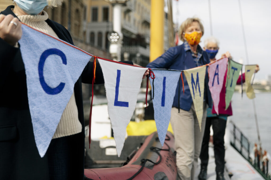 KlimaSeniorinnen activsts hold a multicoloured homemade banner reading 'climate' on the edge of a dock