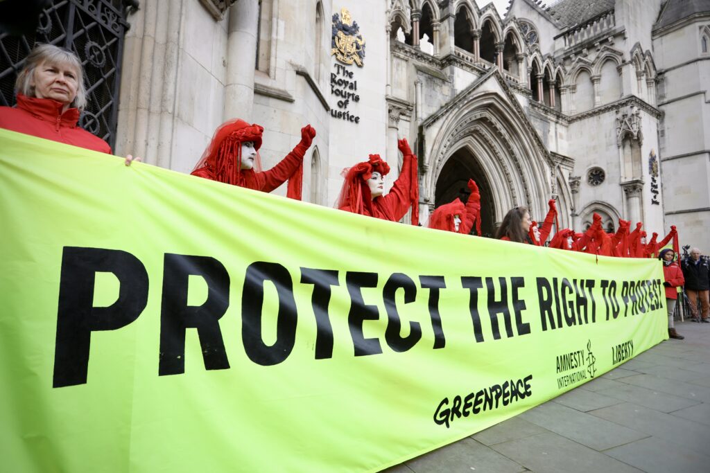 Women wearign red hold a sign reading 'protect the right to protest', in front of the Royal Courts of Justice, London
