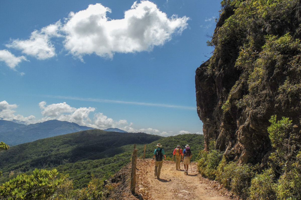 3 hikers on the Camino de Costa Rica trail with blue skies and views on tree covered mountains