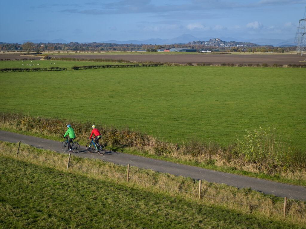 Two cyclists on a path between two expansive, green fields