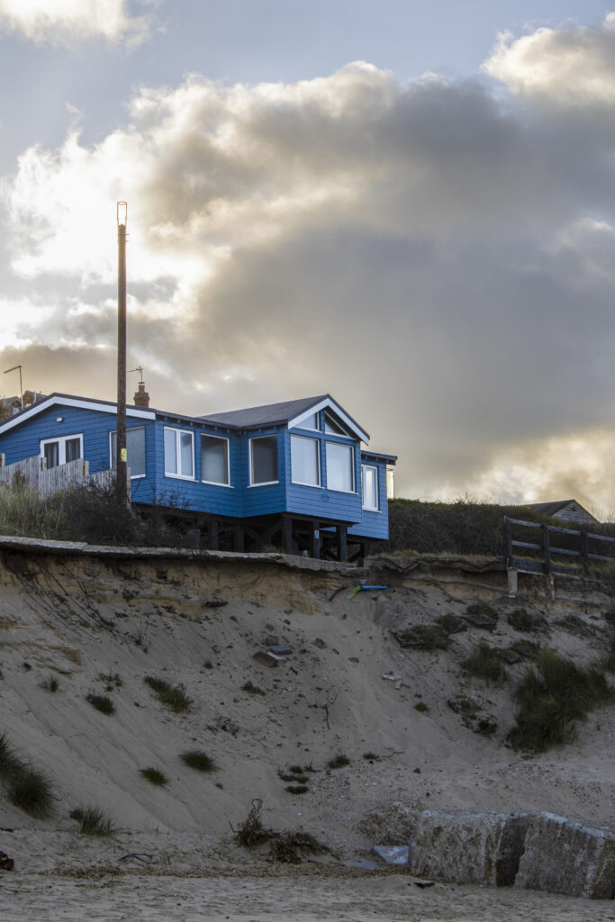Blue wooden house on the edge of a sand dune in front of a gloomy sky