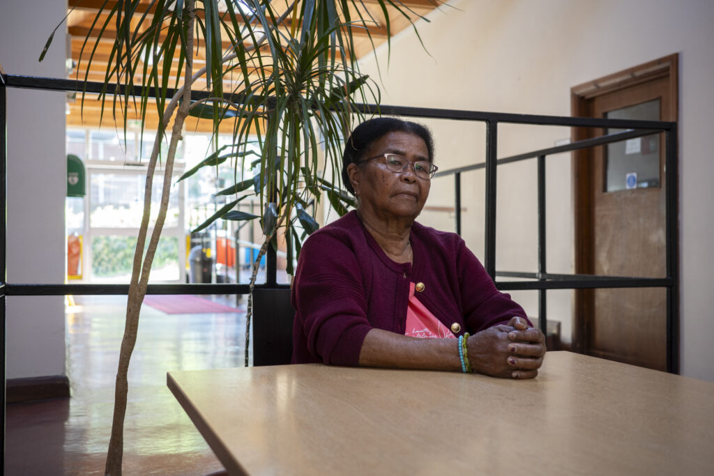 Elderly woman sits at a table and looks at camera with pained look.