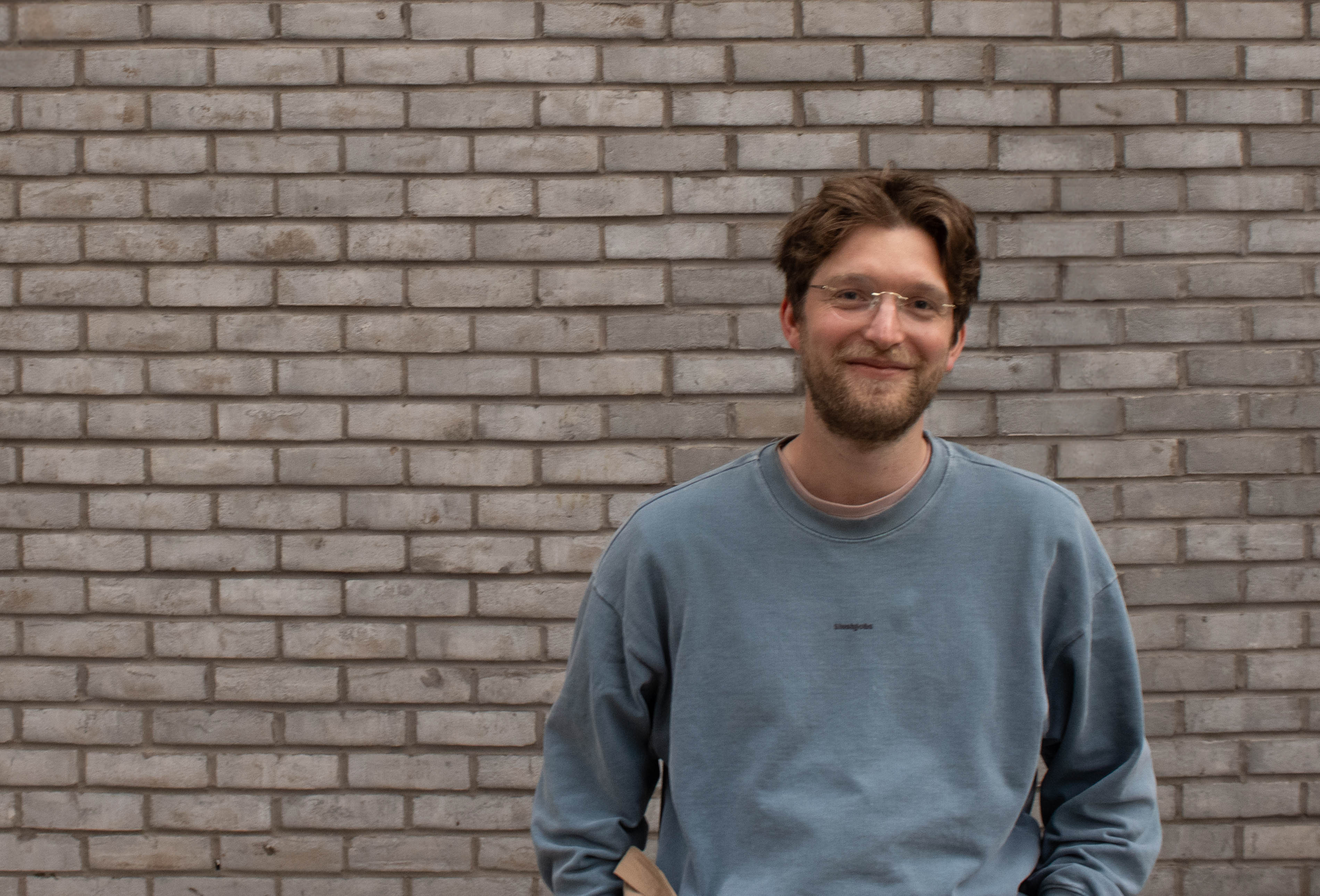 A man faces the camera with a brick background