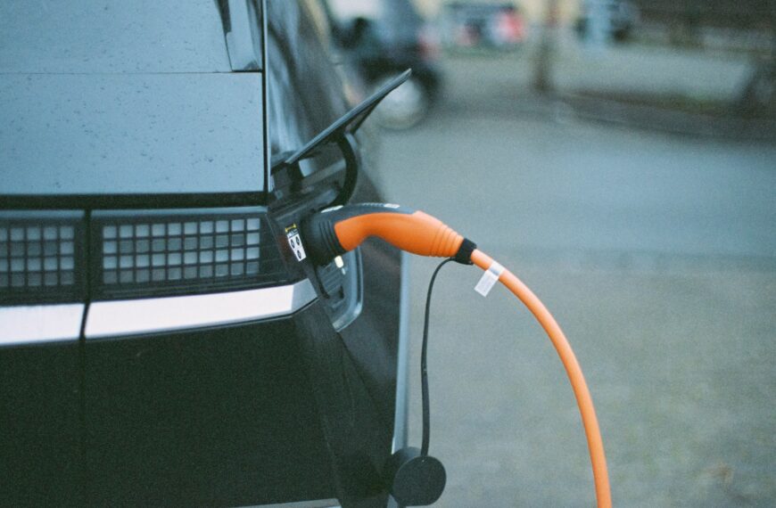 A black electric car charges with an orange cable