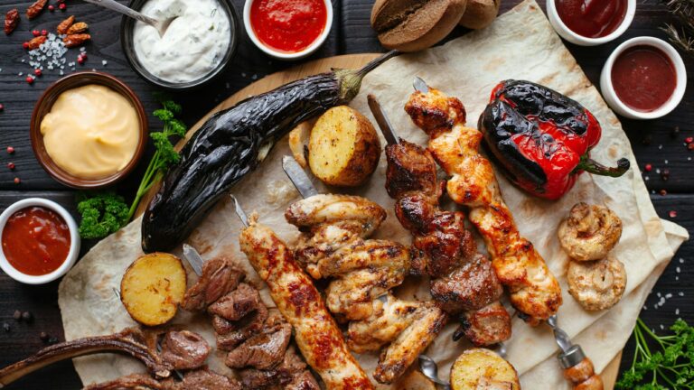 A table of food, with meat skewers, red peppers, aubergines and condiments