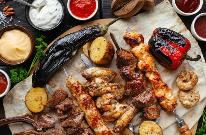 A table of food, with meat skewers, red peppers, aubergines and condiments